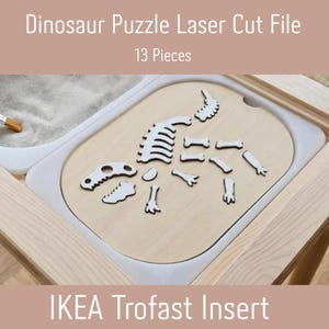 May include: A light-colored wooden dinosaur puzzle laser cut file with 13 pieces, designed as an IKEA Trofast insert. The puzzle pieces form a skeleton shape and are arranged on a flat, oval-shaped wooden board within a white plastic tray.
