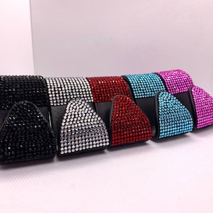 May include: Five decorative hooks with a triangular shape, covered in rhinestones. The hooks are in black, silver, red, blue, and pink.