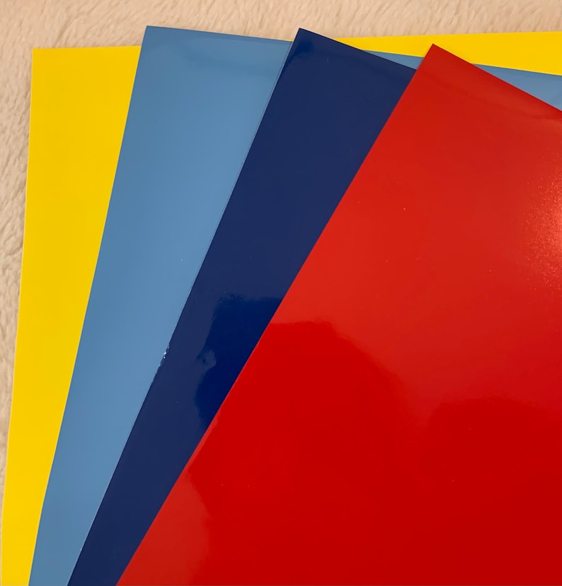 May include: A collection of glossy, colored sheets arranged in a fan shape. The colors include yellow, light blue, dark blue, and red. The sheets have a reflective surface, suggesting a vinyl or similar material.