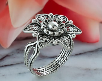 May include: A silver ring with a delicate floral design. The ring is made of filigree and has a round center stone.