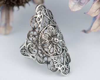 May include: A silver filigree ring with a large flower design. The ring is delicate and intricate, with a lot of detail.