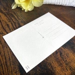 May include: A white rectangular postcard with a textured surface. The back features a stamp box, address lines, and the text NINE EIGHT designs by Sarah Spink. A small number 8 is printed in the bottom left corner and a social media handle is included.