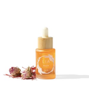May include: A small amber glass bottle of face oil with a wooden cap and dropper. The bottle has a white label with the word "LIA" and "Face Oil" printed on it. Dried rosebuds and saffron threads are scattered near the bottle.