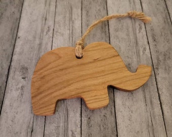 Pode incluir: Um ornamento de elefante de madeira com acabamento em madeira natural e um cordão para pendurar.