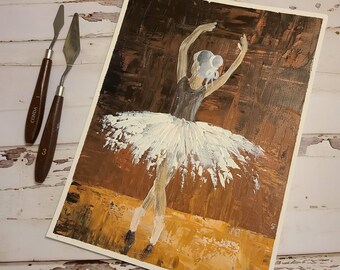 May include: A painting of a ballerina in a white tutu, with a brown background. The ballerina is in mid-pose, with her arms raised above her head. The painting is signed "SLAU" in the bottom right corner.