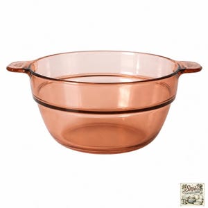 Könnte beinhalten: Eine durchscheinende bernsteinfarbene Glasschale mit einem breiten, kreisförmigen Rand und zwei kleinen, integrierten Seitengriffen. Die Schale hat einen glatten, abgerundeten Boden und eine deutliche horizontale Rille um die Außenwand.