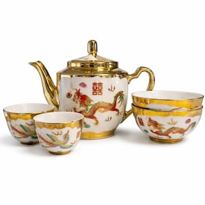 May include: A white and gold porcelain tea set featuring a teapot and four cups. The teapot and cups are decorated with a red and gold dragon design. The set has gold trim and handles.