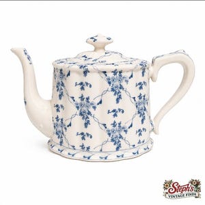 Peut inclure: Une théière en céramique de couleur crème ornée d'un motif floral bleu avec un design en treillis. La théière possède un bec verseur incurvé, une anse robuste et un couvercle assorti avec un bouton. Le corps présente des cannelures verticales.