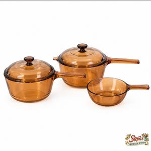 Peut inclure: Un ensemble de trois ustensiles de cuisine en verre ambré composé de deux casseroles avec couvercle et d'une poêle ouverte. Chaque pièce présente un corps rond, un long manche et une teinte brune transparente. Les couvercles ont des boutons en verre.
