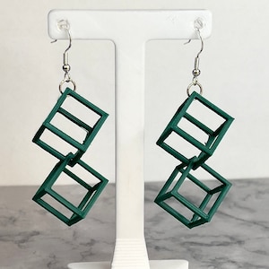 May include: A pair of green geometric cube earrings. Each earring is made of two interlocking cubes.