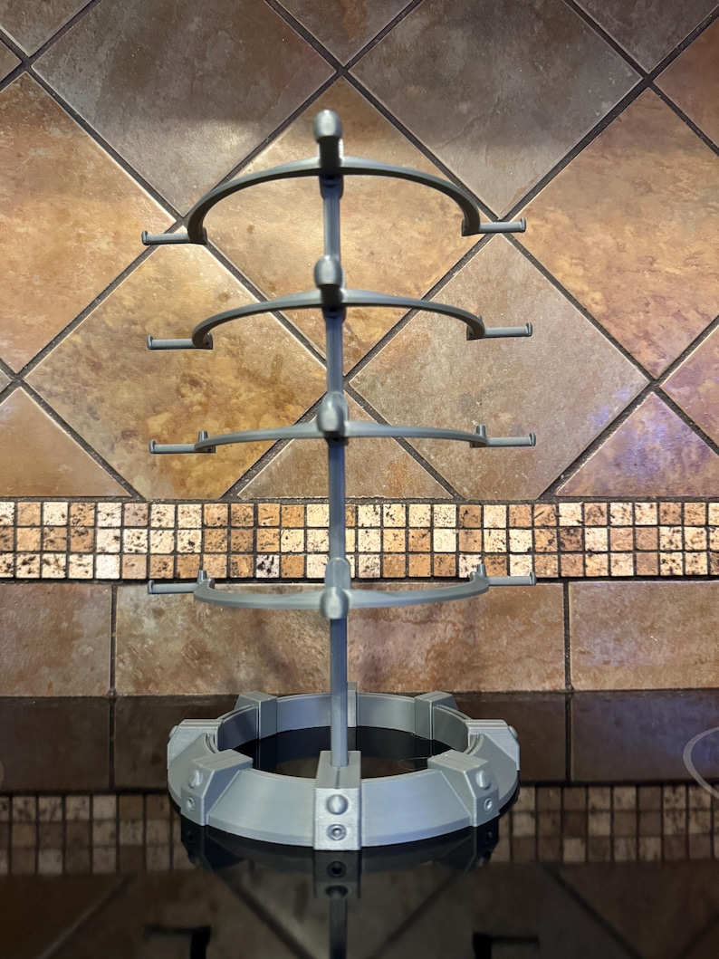 May include: A gray, multi-tiered display stand with a circular base and four curved arms. The stand is made of a matte material and is designed to hold items. The stand is approximately 12 inches tall.