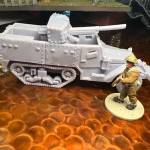 Puede incluir: Modelo gris en miniatura de un vehículo militar con un cañón largo y una figura de soldado en miniatura con uniforme beige y casco verde. El vehículo tiene una base de orugas y remaches detallados.