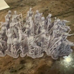 May include: A collection of small, pale purple figurines, likely miniatures for a tabletop game. The figures are closely arranged and seem to be in different poses, possibly depicting a battle. The base is a light purple colour.
