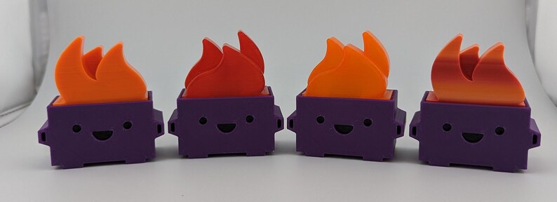 May include: Four purple and orange 3D printed figurines of a trash can with a smiling face and flames on top.