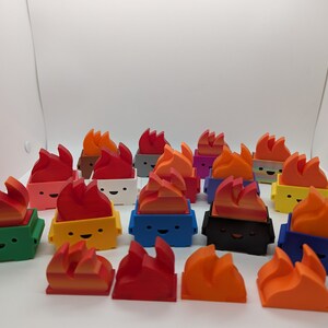 May include: A collection of 18 small, colorful, 3D printed figurines shaped like trash cans with flames on top. The figurines have different colored bodies and flames, including green, yellow, blue, black, white, red, orange, and purple.
