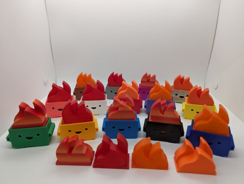 May include: A collection of 18 small, colorful, 3D printed figurines shaped like trash cans with flames on top. The figurines have different colored bodies and flames, including green, yellow, blue, black, white, red, orange, and purple.