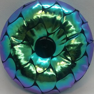 May include: A round, iridescent green and purple pillow with a black center and a black and white geometric pattern.