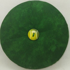 May include: A green fabric pincushion with a tennis ball button in the center.