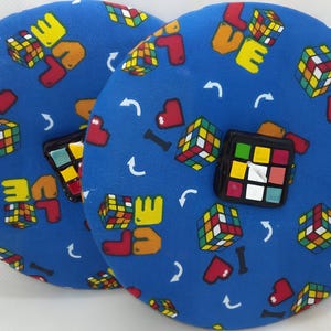 May include: Two blue round cushions with a repeating pattern of colorful Rubik's cubes, hearts, and the word "LOVE" in a pixelated font. The cushions have a large Rubik's cube in the center.