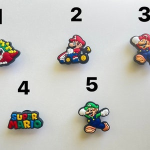 Könnte beinhalten: Fünf bunte Schuhcharms mit Figuren aus der Super Mario Videospiel-Reihe. Die Charms zeigen Mario, Luigi, Bowser, ein Super Mario Logo und Mario in einem Rennwagen.