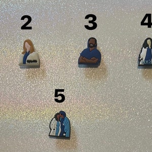 Puede incluir: Cinco charms de zapatos diferentes con personajes de Grey's Anatomy. Los charms están hechos de un material suave y flexible y presentan la imagen de Meredith Grey, Derek Shepherd, Miranda Bailey, Alex Karev y una pareja de personajes.
