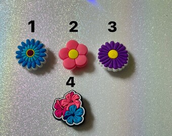 May include: Four colorful flower shoe charms. The charms are numbered 1 through 4. Charm 1 is a blue flower with a white center. Charm 2 is a pink flower with a yellow center. Charm 3 is a purple flower with a yellow center. Charm 4 is a multi-colored flower with pink, blue, and white petals.