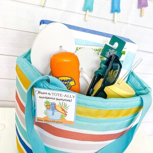 May include: A blue and white striped tote bag filled with summer essentials, including flip flops, sunscreen, sunglasses, a straw, and a yellow tumbler. A gift tag with the text "Have a TOTE-ALLY awesome summer! from Matthew" is attached to the bag.