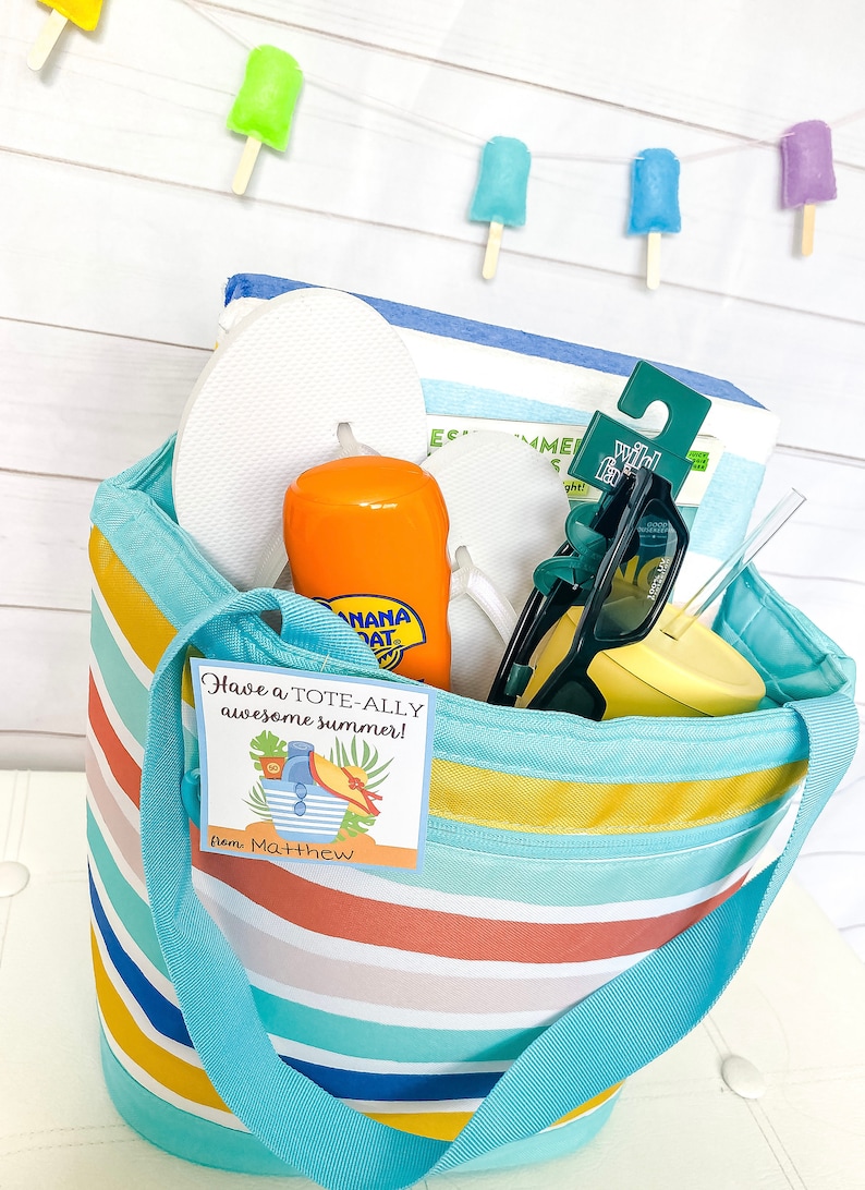 May include: A blue and white striped tote bag filled with summer essentials, including flip flops, sunscreen, sunglasses, a straw, and a yellow tumbler. A gift tag with the text "Have a TOTE-ALLY awesome summer! from Matthew" is attached to the bag.