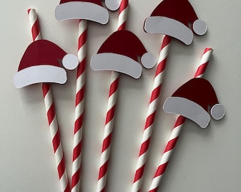 May include: Six red and white striped paper straws with Santa hat decorations. The Santa hats are red with white trim and a white pom-pom. The straws are arranged in a fan shape against a white background.