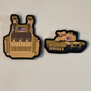 Puede incluir: Dos parches de goma de color marrón claro y negro. Uno es un chaleco táctico con una bandera estadounidense en la parte delantera. El otro es un tanque con una bandera estadounidense en el lateral y las letras "FJB" en la parte trasera.
