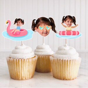 May include: Three cupcakes with white frosting topped with colorful cupcake toppers featuring a child in a pool float. One topper shows a child in a pink flamingo float, another shows a child in a blue and pink tube float, and the last topper shows a child's face wearing heart-shaped sunglasses.