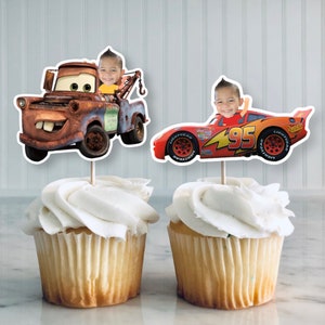 May include: Two cupcake toppers featuring characters from the Disney Pixar movie Cars. One topper is a red race car with the number 95 on the side and the other is a rusty orange tow truck. Both toppers have a child's face superimposed on the driver.
