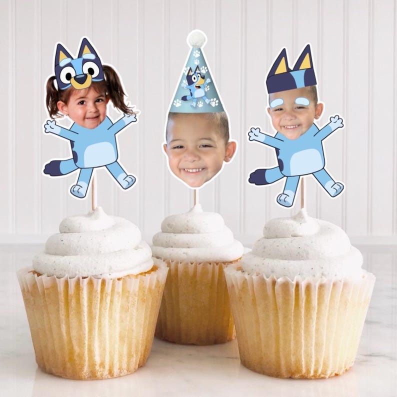 Peut inclure: Trois d&eacute;corations de cupcake bleu et blanc repr&eacute;sentant un personnage de chien de dessin anim&eacute; avec le visage d'un enfant dans l'espace de la t&ecirc;te. Les d&eacute;corations sont sur des cure-dents et sont sur des cupcakes avec du gla&ccedil;age blanc.