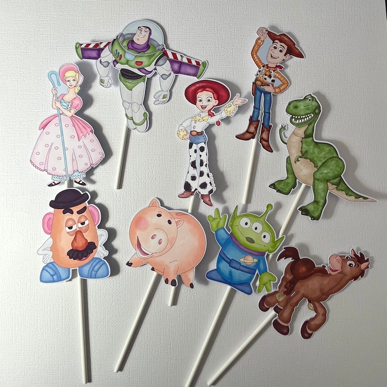May include: A collection of eight paper character cutouts attached to white sticks, featuring colorful illustrations of a pink-dressed shepherd, a space ranger, a cowgirl, a cowboy, a green dinosaur, a potato figure, a pig, an alien, and a brown horse.