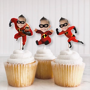 May include: Three cupcakes with white frosting topped with edible images of a superhero character from the movie Incredibles. The character is wearing a red and black suit and has a black mask.