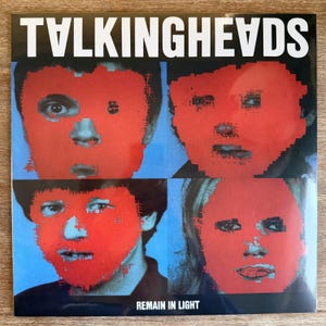 May include: Album cover for Talking Heads' "Remain in Light." The artwork shows four pixelated faces with red masks on a blue backdrop. The band's name is in white block letters at the top, and the album title is at the bottom.