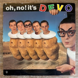 May include: Album cover for the band Devo, featuring the text "oh, no! it's DEVO". The image shows five band members with potato bodies and white collars. One band member is wearing glasses and looking at the viewer.