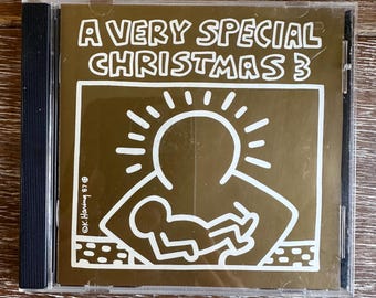 May include: A gold CD case with a white outline of a sun and a person holding a baby. The text "A Very Special Christmas 3" is printed on the front of the case.