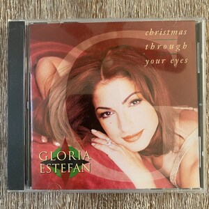 May include: A CD cover featuring Gloria Estefan, with a red background and the title "Christmas Through Your Eyes".