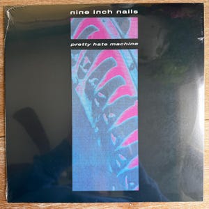 May include: A vinyl record album titled "pretty hate machine" by Nine Inch Nails. The album cover is black with a vertical rectangle featuring a blue and pink abstract design. The band's name is in white text at the top.