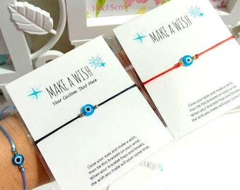 May include: Close-up of several "Make a Wish" bracelets. Each bracelet features a small blue evil eye charm on a colored cord. The cards read "Make a Wish" with instructions. A blue bracelet is worn on a wrist.