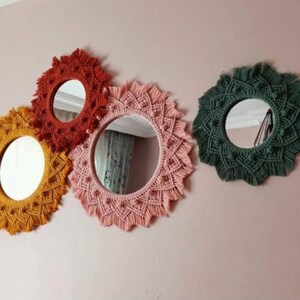 May include: Four round macrame mirrors with different colored yarn. The mirrors are hanging on a pink wall. The mirrors are all different sizes and have a variety of patterns.