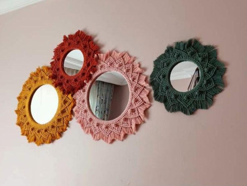 May include: Four round macrame mirrors with different colored yarn. The mirrors are hanging on a pink wall. The mirrors are all different sizes and have a variety of patterns.