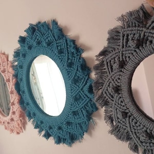 May include: Three round mirrors with macrame frames. The mirrors are different sizes. The largest mirror has a gray frame, the middle mirror has a teal frame, and the smallest mirror has a pink frame.