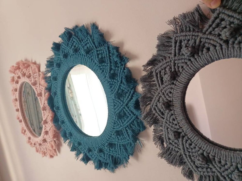 May include: Three round mirrors with macrame frames. The mirrors are different sizes. The largest mirror has a gray frame, the middle mirror has a teal frame, and the smallest mirror has a pink frame.