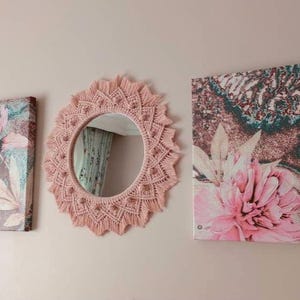 May include: Three wall decor pieces with a floral theme. A pink macrame mirror with a round mirror in the center. Two canvas prints with pink flowers on a brown background.