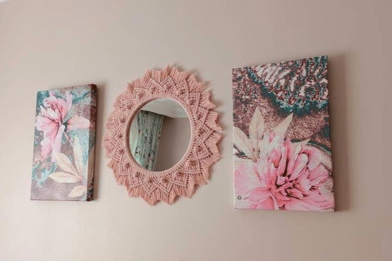 May include: Three wall decor pieces with a floral theme. A pink macrame mirror with a round mirror in the center. Two canvas prints with pink flowers on a brown background.