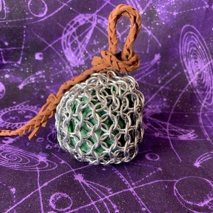 May include: A silver chainmail ball with a brown leather cord. The ball is hanging against a purple background with white stars.
