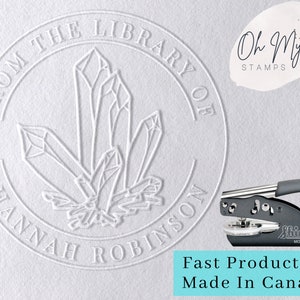 May include: A white embossed library seal with the text "FROM THE LIBRARY OF HANNAH ROBINSON" around a crystal design. The image includes a "Shiny" model seal press and the text "Oh My STAMPS".