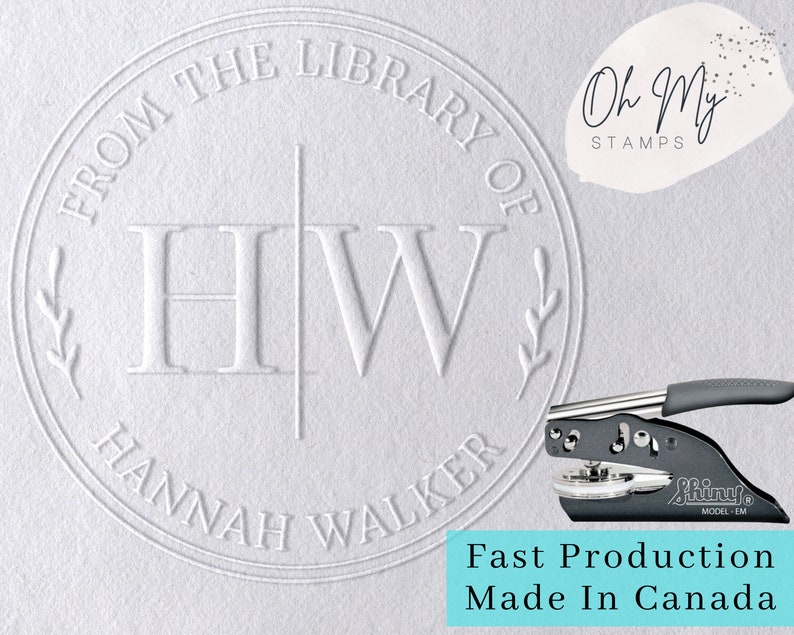 May include: A white round self-inking stamp with the text "From the Library of Hannah Walker" and the initials "HW" in a decorative font. The stamp is made by Oh My Stamps and is labeled "Fast Production Made in Canada".